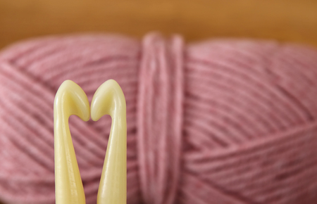 Two needles forming a heart in front of warm and cozy yarn ball of wool backgroundの写真素材