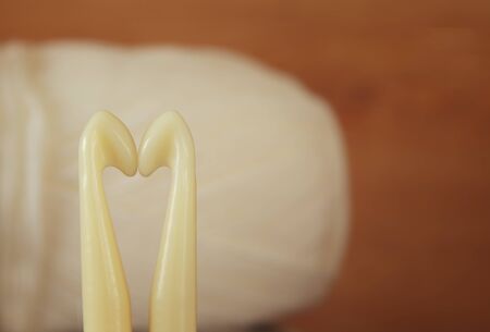 Two needles forming a heart in front of warm and cozy yarn ball of wool background