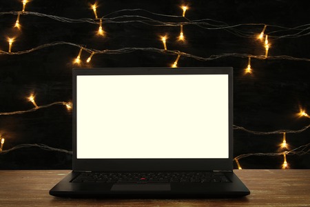 Image of open laptop with white screen on wooden table in front of abstract glitter background. For mockupの写真素材
