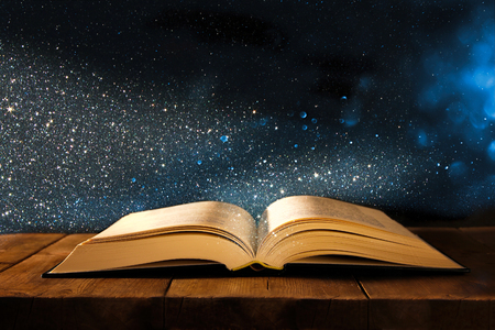image of open antique book on wooden table with glitter overlayの写真素材