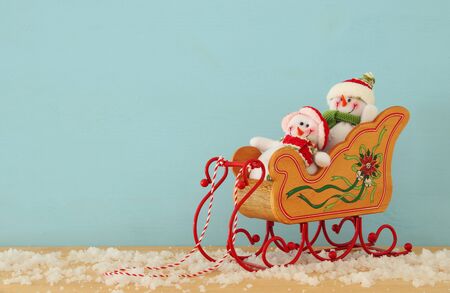 Image of christmas tree and snowmen on the wooden old sled over snowy wooden table