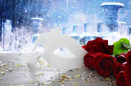 Valentines day romantic background with beautiful bouquet of roses and masquerade white mask on wooden tableの写真素材