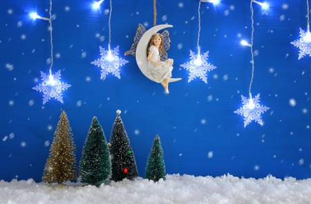 Christmas trees, snowflakes silver garland light, fairy on the moon over the snow and blue backgroundの写真素材