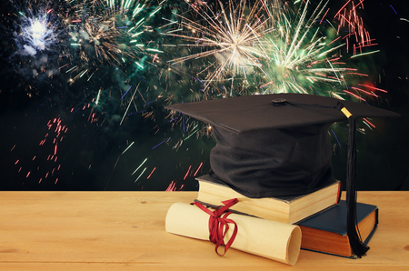 Image of graduation black hat over old books next to graduation on wooden desk. Education and back to school conceptの写真素材