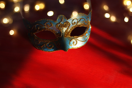 Image of elegant blue and gold venetian, mardi gras mask over red background. Magical glitter ovrlayの写真素材
