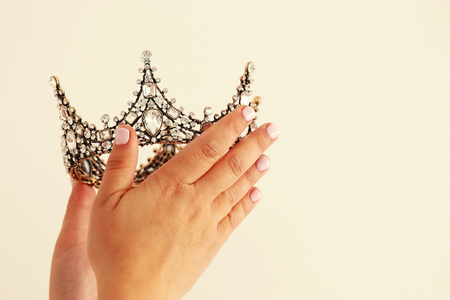 Woman's hand holding a crown for show victory or winning first place. White background. Copy space. Isolatedの写真素材