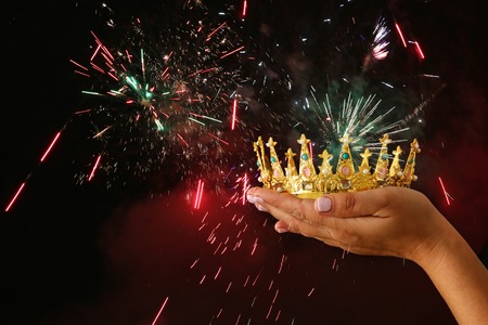 Woman's hand holding a crown for show victory or winning first place over black background with...