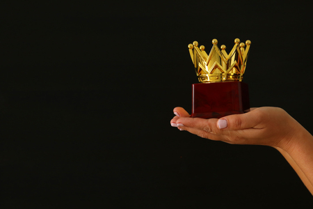 Woman's hand holding a crown trophy for show victory or winning first place over black backgroundの写真素材