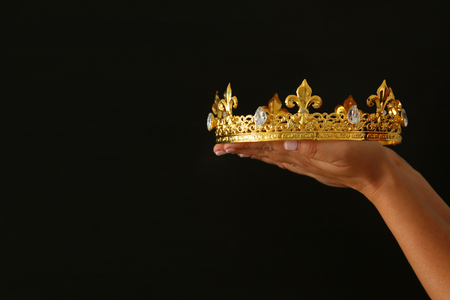 Woman's hand holding a crown for show victory or winning first place over black backgroundの写真素材