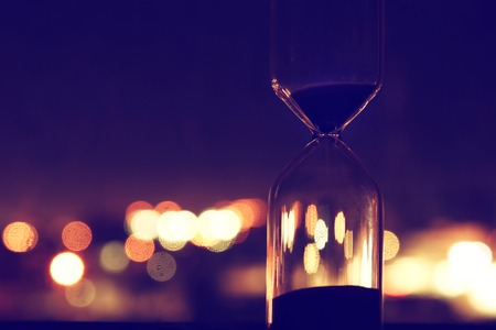 Hourglass over bokeh city lights as time passing concept for business deadline