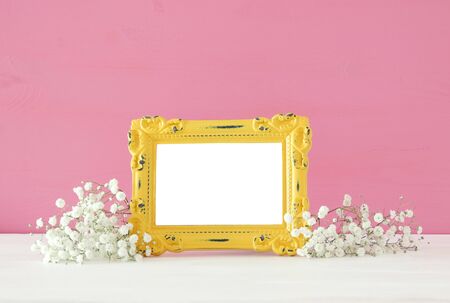 Image of beautiful bouquet of spring flowers next to blank vintage photo frame on wooden table. For...