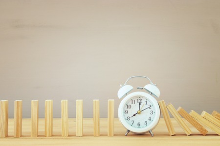 A clock stopping the domino effect. retro style image executive and risk control concept