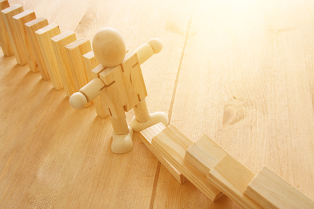 A wooden dummy stopping the domino effect. retro style image executive and risk control conceptの写真素材
