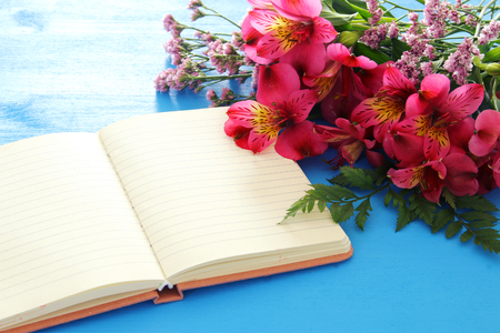 Top view of red beautiful flowers arrangement and empty open notebook over blue wooden background. Copy spaceの写真素材