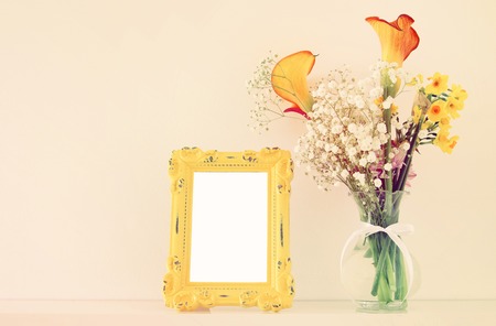 Image of beautiful bouquet of yellow spring flowers next to blank vintage photo frame over white table. For photography mock up montageの写真素材