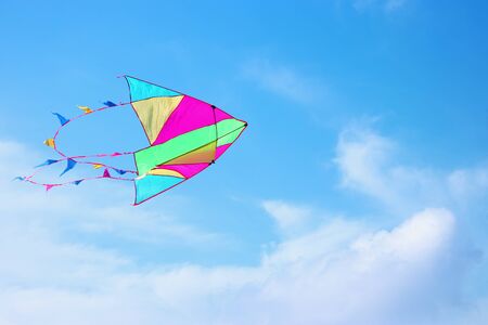 Colorful kite flying in the blue sky through the clouds.の写真素材
