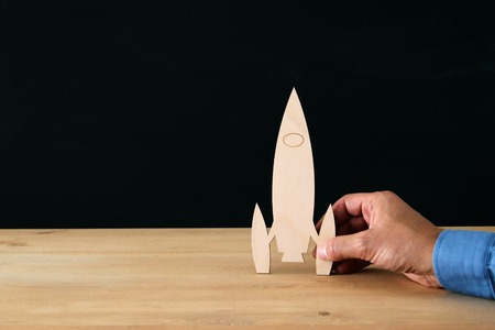 man's hand holding wooden rocket, over black background