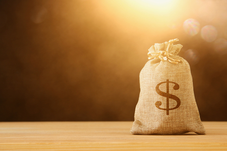A sack of money over wooden desk and glitter black backgroundの写真素材