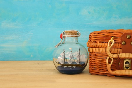 nautical concept image with sail boat in the bottle and old wicker suitcase box over wooden table. Selective focusの写真素材
