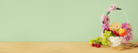 image of fruits and cheese in decorative basket with flowers over wooden table. Symbols of jewish holiday - Shavuotの写真素材