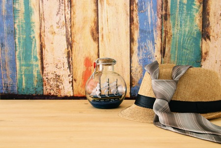 Image of male fedora hat and boat in the bottle over wooden table. Father's day conceptの写真素材