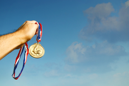 man hand raised, holding gold medal against sky. award and victory conceptの写真素材