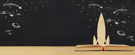 Back to school concept. wooden rocket and space sketchs over open book in front of classroom blackboardの写真素材