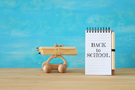 Back to school concept. Wooden toy car with colorful pencils on the roof next to notebookの写真素材