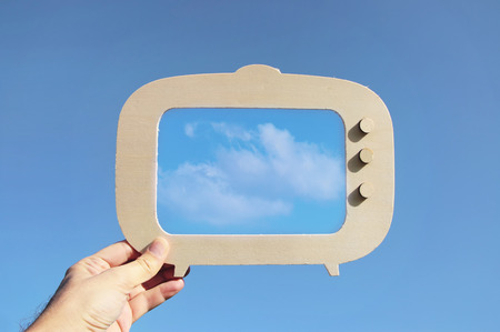 image of hand holding tv frame in front of sky with cloud. capture the moment or minimal concept