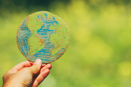 man hand holding earth globe in front of outdoor green bokeh backgroundの写真素材