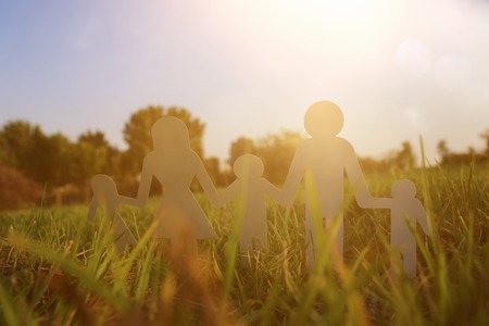 image of happy family concept. paper cut people holding hands together in green grass during sunsetの写真素材