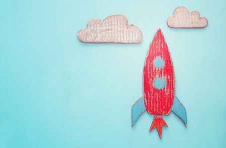 Rocket cut from cardboard and painted over wooden blue backgroundの写真素材