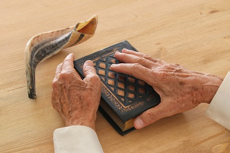 Old Jewish man hands holding a Prayer book, praying, next to shofar (horn). Jewish traditional symbols. Rosh hashanah (jewish New Year holiday) and Yom kippur conceptの写真素材