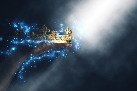 mysteriousand magical image of woman's hand holding a gold crown over gothic black background. Medieval period conceptの写真素材
