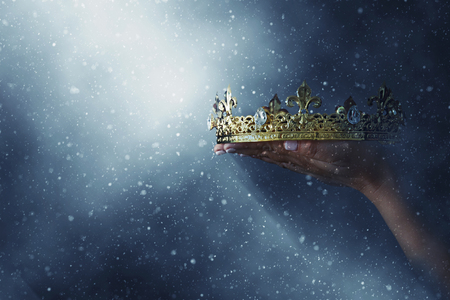 mysteriousand magical image of woman's hand holding a gold crown over gothic black background. Medieval period conceptの写真素材