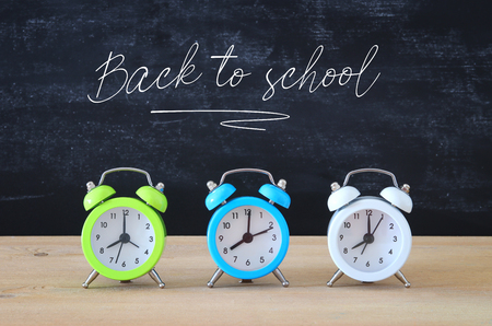 A collection of colorful alarm clocks over wooden desk in front of blackboardの写真素材