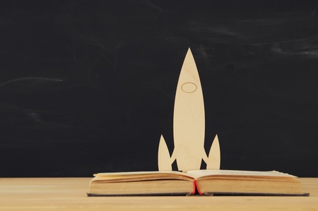 Back to school concept. wooden rocket over open book in front of classroom blackboardの写真素材