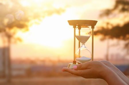 Young woman holding Hourglass during sunset. vintage styleの写真素材