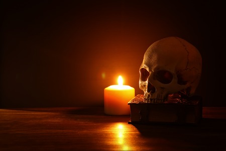 Human skull, old book and burning candle over old wooden table and dark backgroundの写真素材