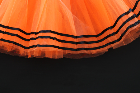 Halloween holiday minimal top view image of orange tulle skirt costume over black wooden background. Copy spaceの写真素材