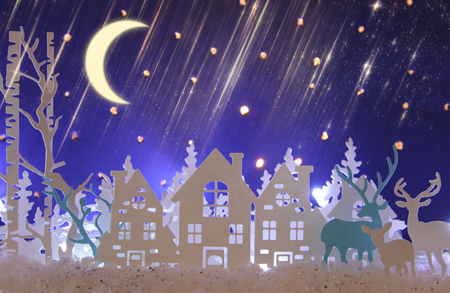 Magical Christmas paper cut winter background landscape with houses, trees, deer and snow in front of night starry sky backgroundの写真素材