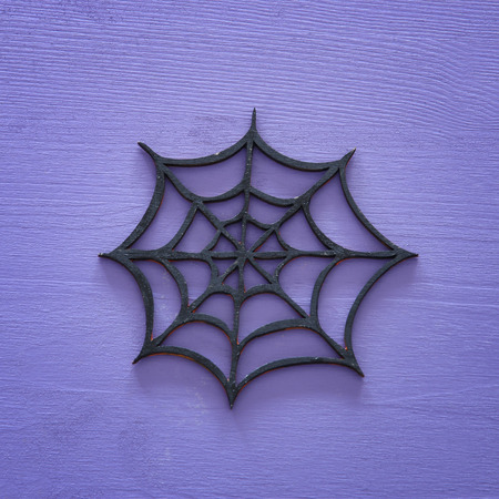 Halloween holiday minimal top view image of spider cobweb over purple wooden background