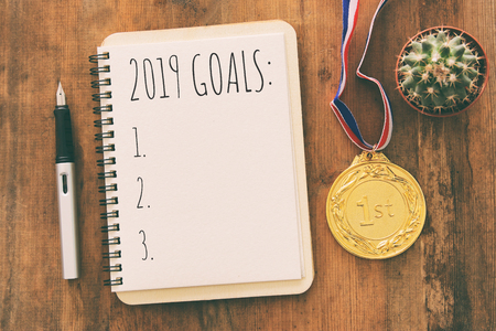 Top view 2019 goals list with notebook over wooden desk