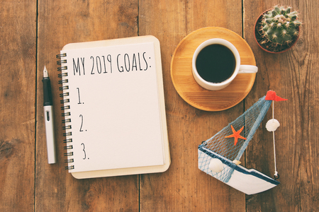 Top view image of 2019 goals list with notebook, cup of coffee over wooden desk