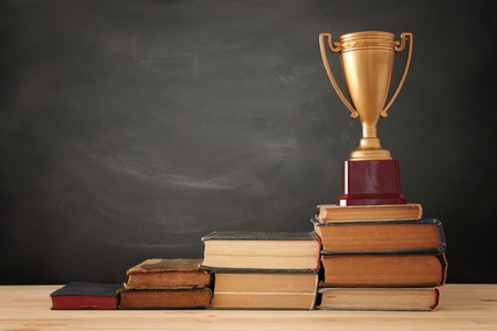 A concept image of education success, a stack of books arranged like a pyramid with golden trophy on topの写真素材