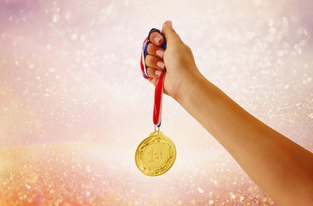 woman hand raised, holding gold medal against glitter background. award and victory conceptの写真素材