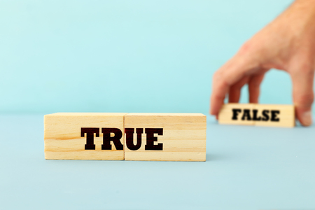 true or false concept man hand picking wooden cubes with text over wooden blue backgroundの写真素材