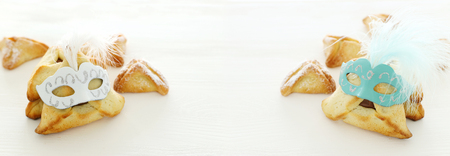 Purim celebration concept (Jewish carnival holiday). Traditional hamantaschen cookies with cute mask over white wooden tableの写真素材