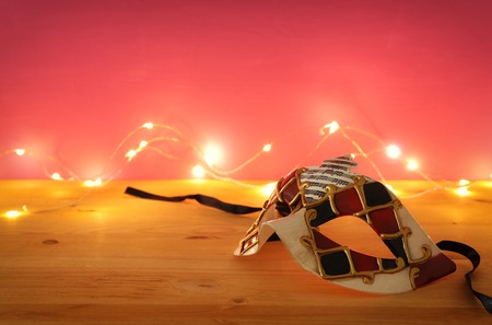 Photo of elegant venetian, mardi gras mask over wooden table and pink background with garland gold lightsの写真素材