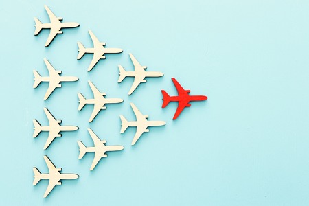 Leadership concept with airplanes on blue wooden background. One red leader flays ahead others.